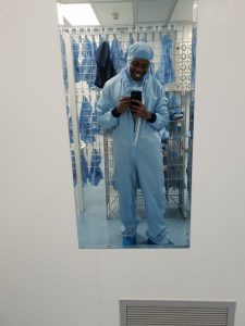 A mirror selfie in a Bioengineering lab by De-Shaine. He is wearing full Personal Protective Equipment including a jumpsuit with a hood
