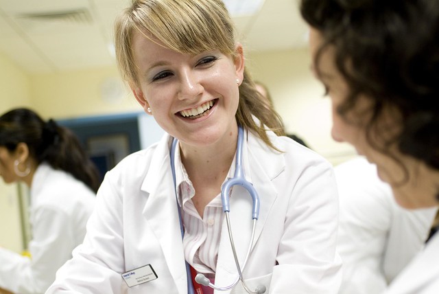 A photograph of a female doctor smiling in discussion with another female doctor. 
