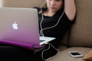 A girl at an apple mac laptop on a sofa with earphones in