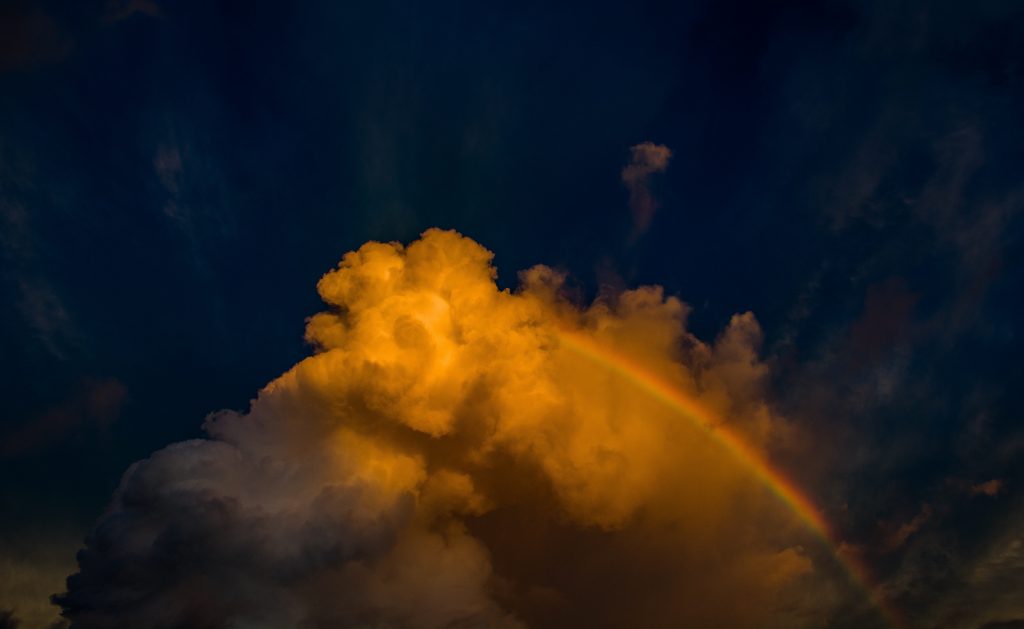A rainbow emerging from clouds on a black background