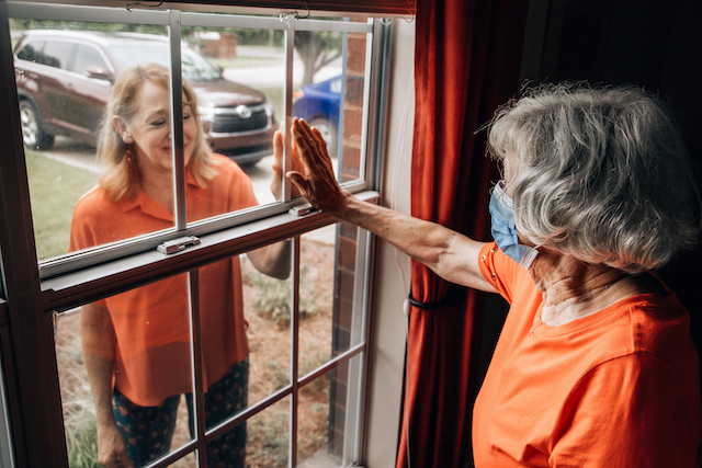Woman with dementia reaching out to another woman through a window