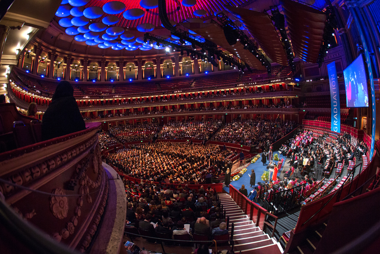 President of Imperial, Professor Alice P. Gast, shakes the hand of a graduating student on the stage at the Royal Albert Hall, while a spectator in a headscarf watches on from the left of the picture.
