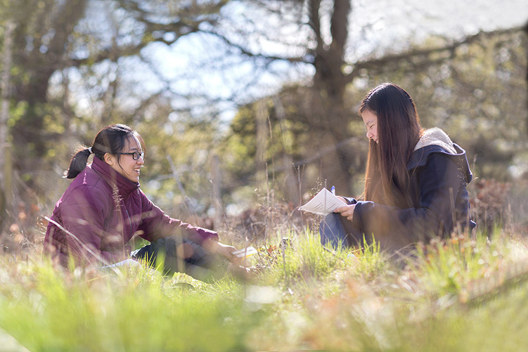 Two students sitting in a field and writing notes