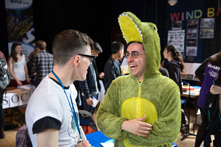 A student dressed in a crocodile costume laughs with a friend at the Freshers' Fair.