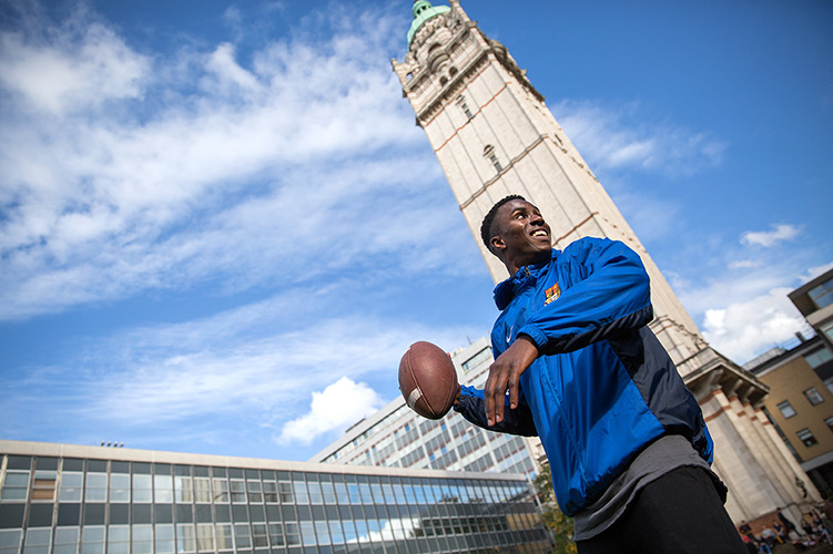 A student about to throw an American football, with the Queen's Tower in the background.
