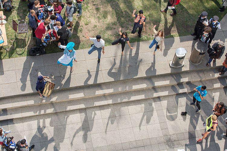 Five students dancing on the Queen's Lawn cast shadows across the terrace.
